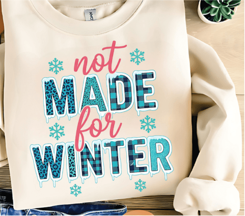 Beige sweatshirt with 'not made for winter' text and snowflake graphics on a wooden surface.