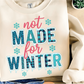Beige sweatshirt with 'not made for winter' text and snowflake graphics on a wooden surface.